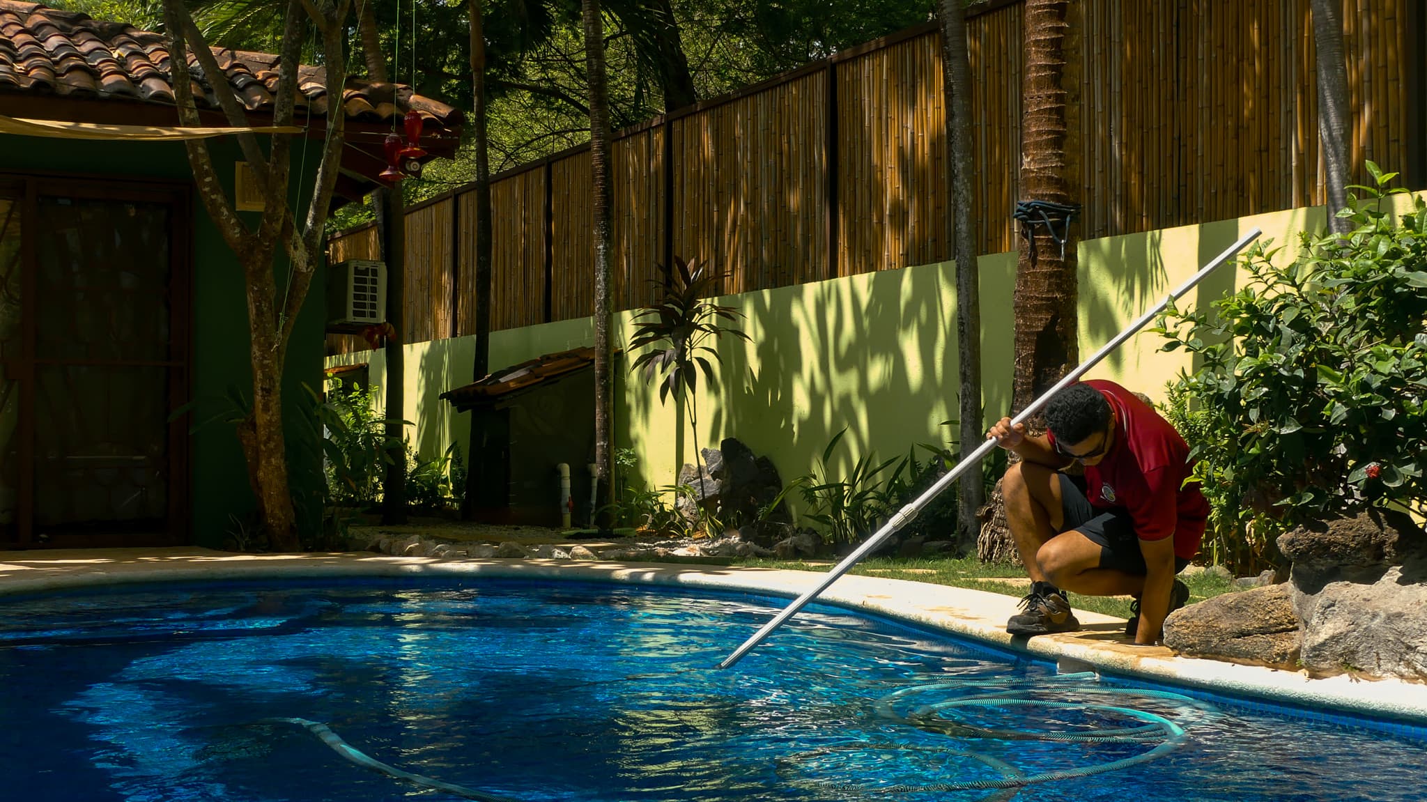 Integrante de Butterfly realizando mantenimiento en una piscina rodeada de jardín.